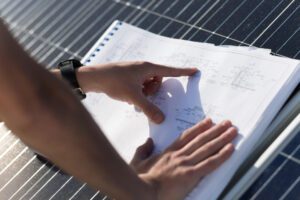 Mãos de um profissional analisando plantas técnicas em papel sobre um painel solar.