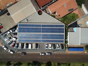 Vista aérea de um prédio comercial com painéis solares instalados no telhado e estacionamento com carros ao redor.