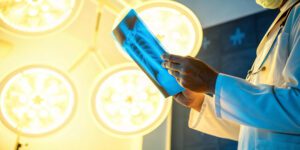 Médico segurando uma radiografia em uma sala cirúrgica iluminada, observando atentamente a imagem do tórax do paciente.