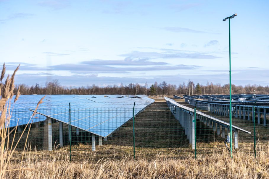 Electric farm with panels for producing clean ecologic energy. Parque solar com fileiras de painéis fotovoltaicos instalados em um campo cercado, em dia claro com céu azul e nuvens.