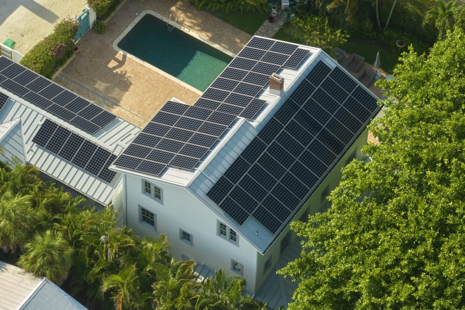 Expensive american residential house with rooftop covered with solar photovoltaic panels for producing of clean ecological electrical energy in suburban rural area. Concept of autonomous home Casa com painéis solares no telhado vista de cima, ao lado de uma piscina.